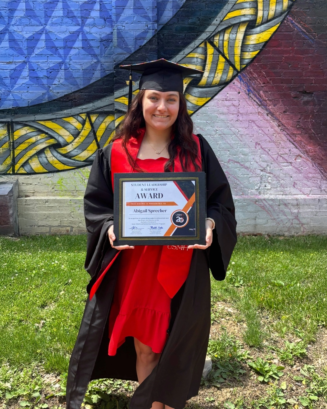 young girl with dark hair in a graduation cap and gown holding an award