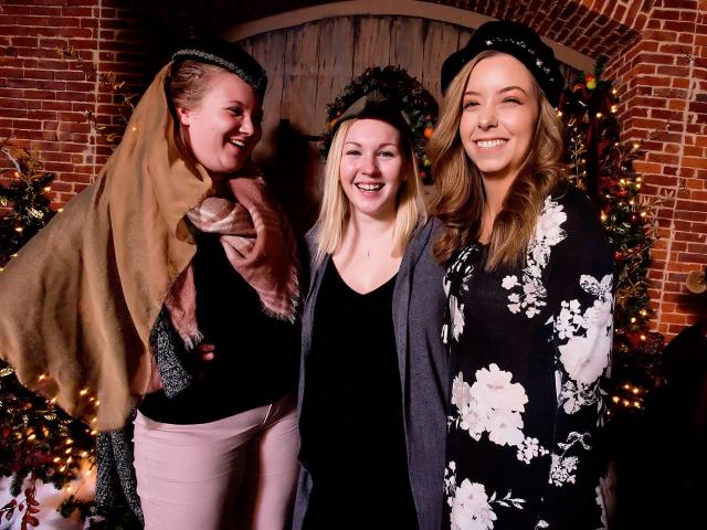 three women laugh while putting on medieval hats