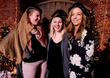 three women laugh while putting on medieval hats